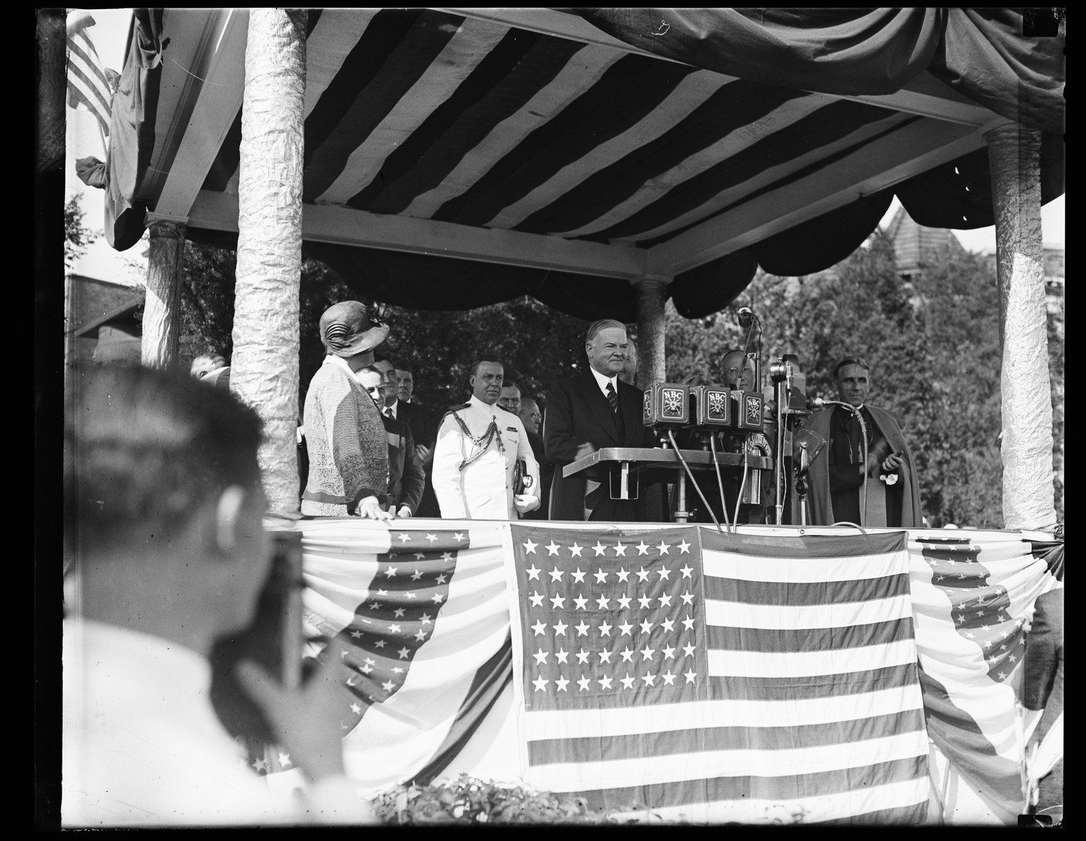 man speaking on gazebo with American flags