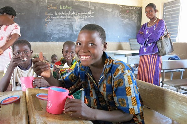 A young boy named Assane smiles in the classroom while eating his yogurt