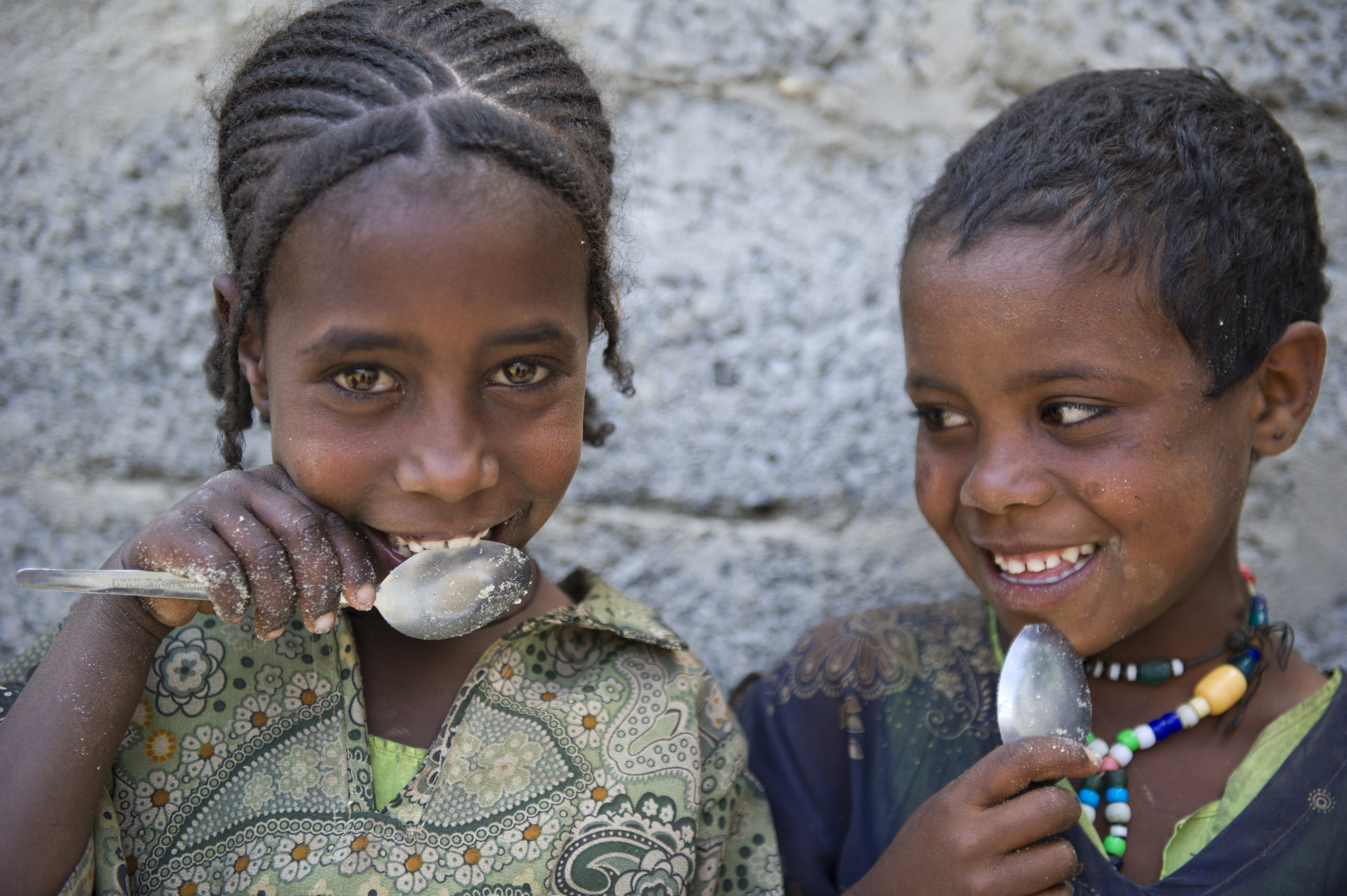 Two kids smiling and holding spoons up to their mouths