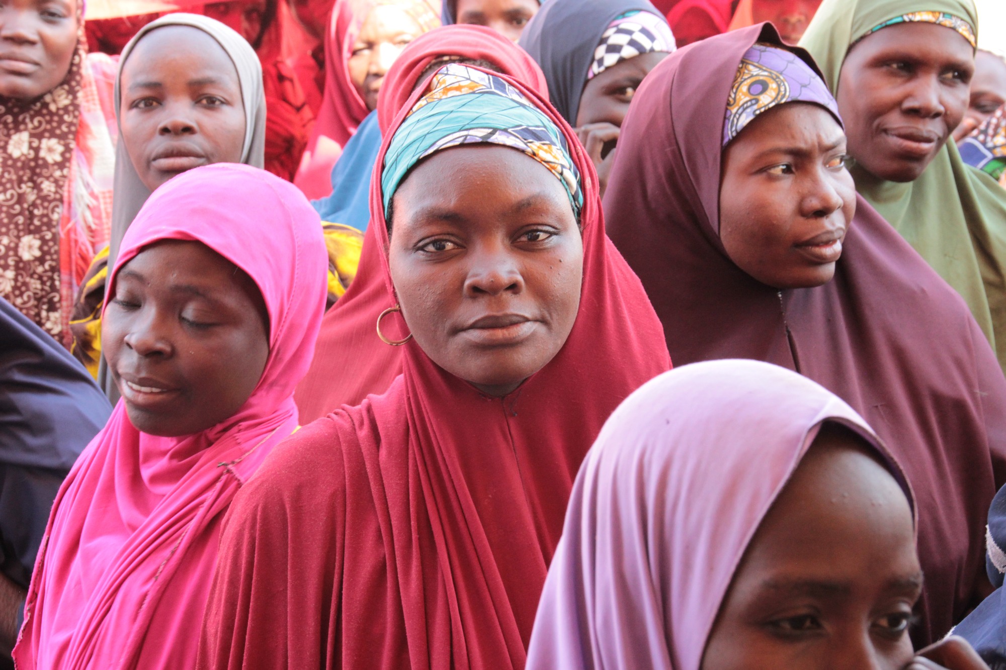 Women at a food distribution center in Nigeria, all wearing brightly colored hijabs on their heads