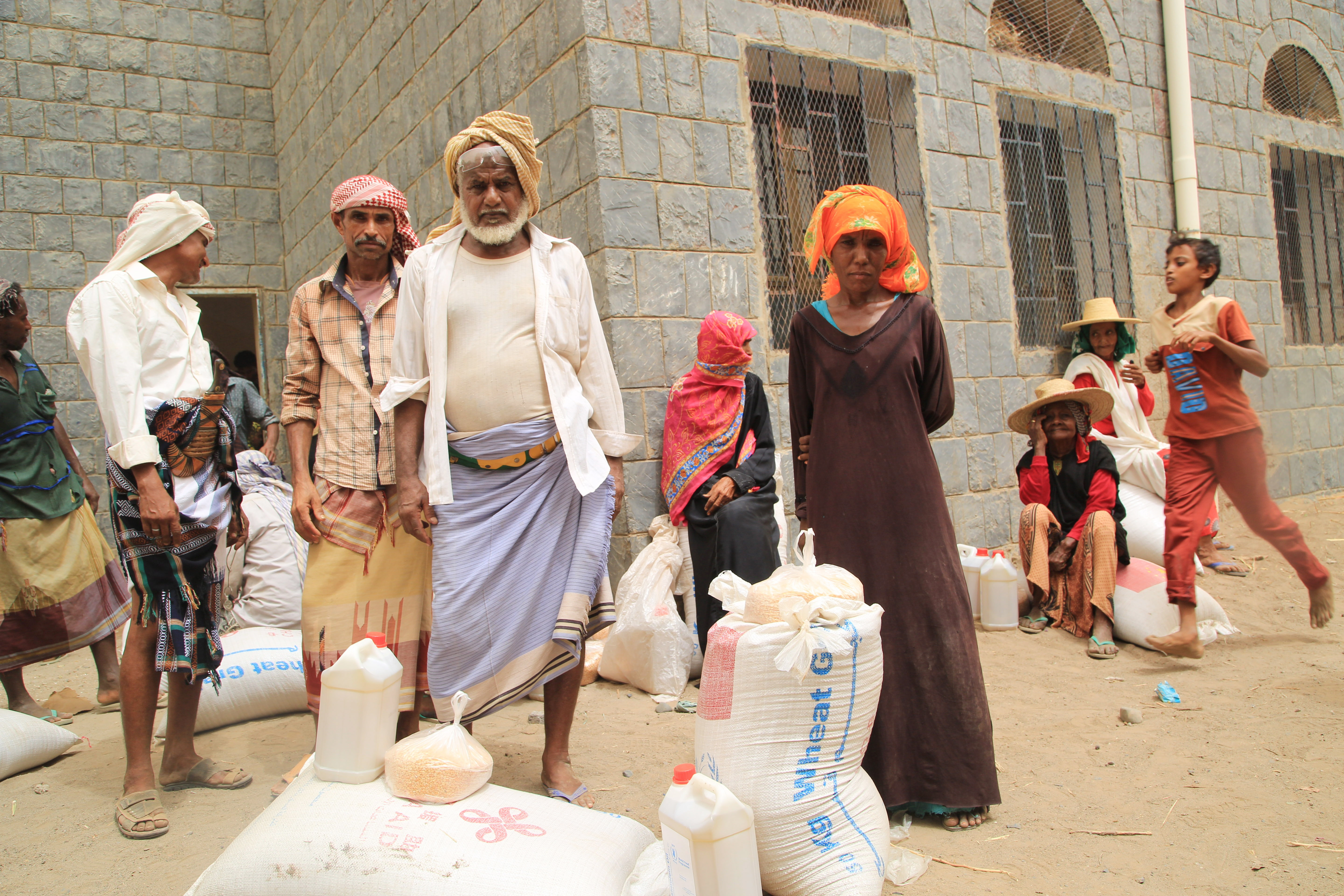 Several people stand with WFP bags and containers in front of them on the ground