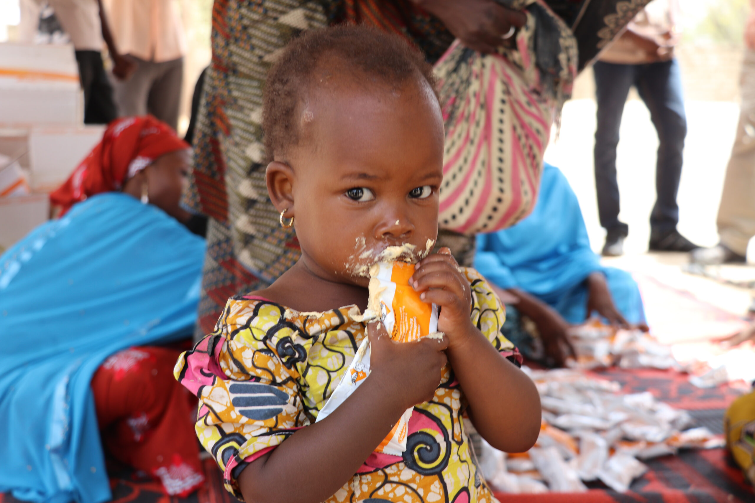 A young girl eats from a Plumpy'Sup packet with food all over her mouth