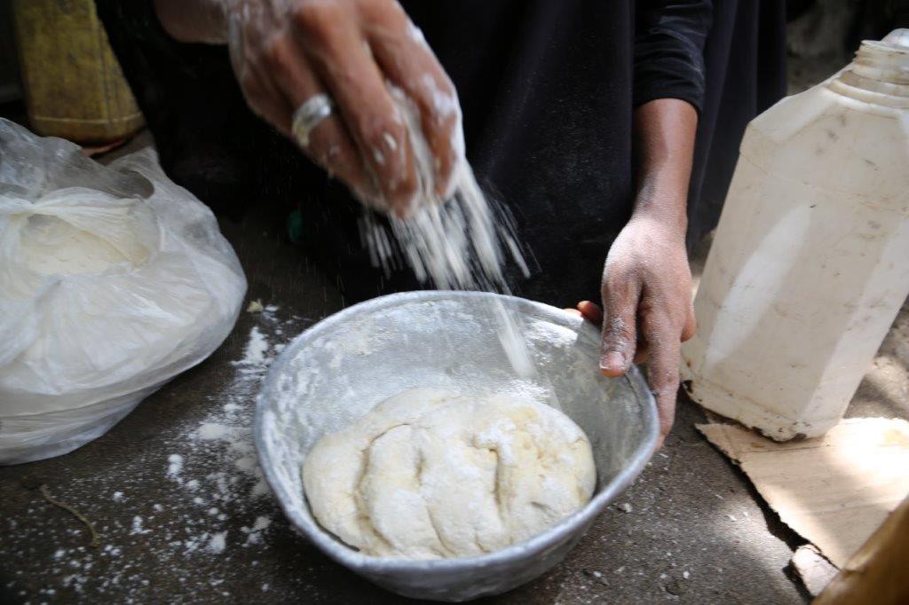 Hands pour flour over tin bowl of dough
