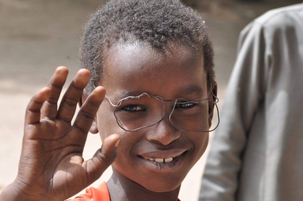 A boy waves at the camera, wearing handmade toy glasses.