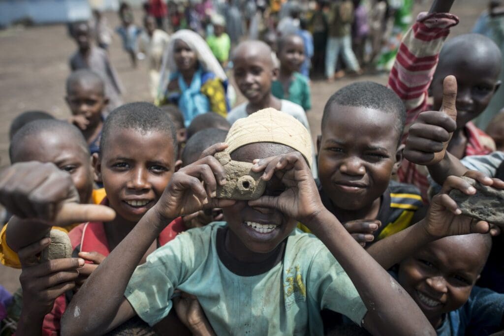 Three young boys look at the camera, one holds up his own clay camera. 