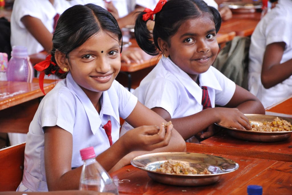 Two young schoolgirls eat a meal at a table.