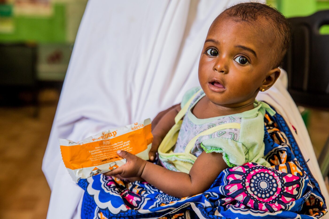 little girl holding peanut bar in mother's lap