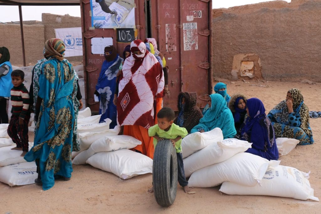 Refugee women and children sit and wait for food at a camp in Algeria