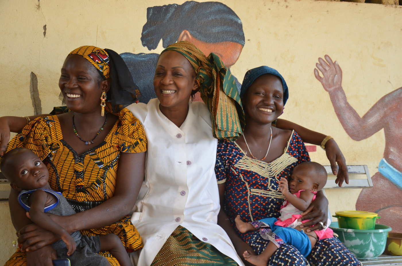 A nurse, laughing, is surrounded by a group of her patients.