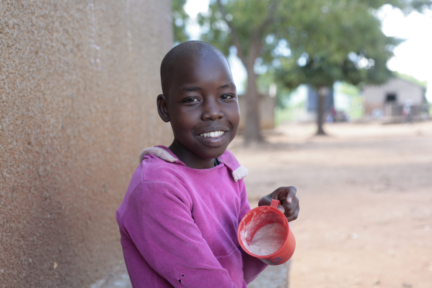 A young girl in Uganda wearing purple smiles for a camera