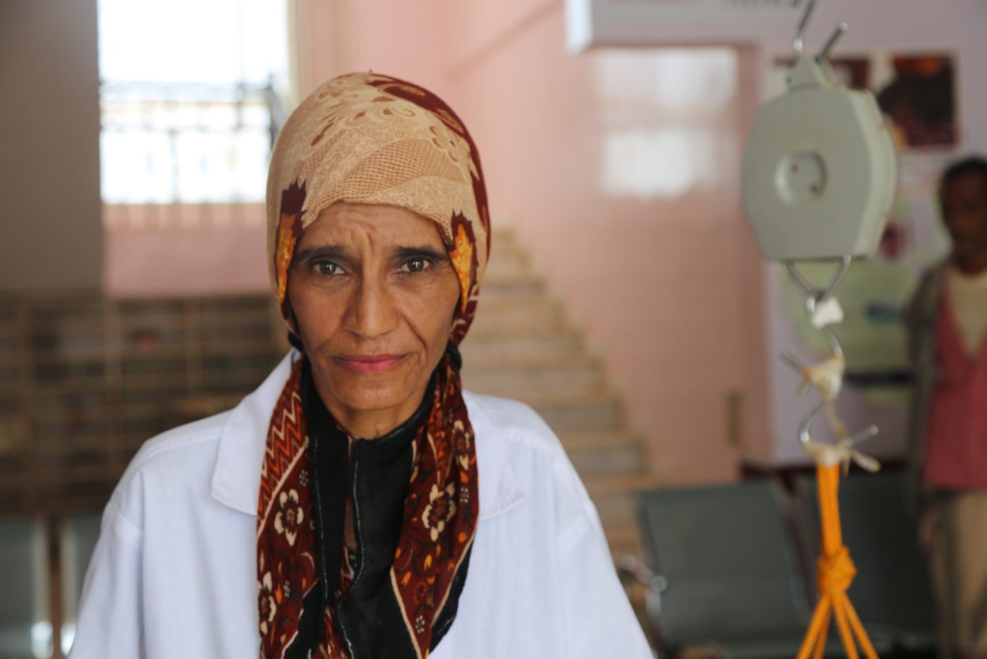 A nurse in a headcover and white scrubs poses for a photograph