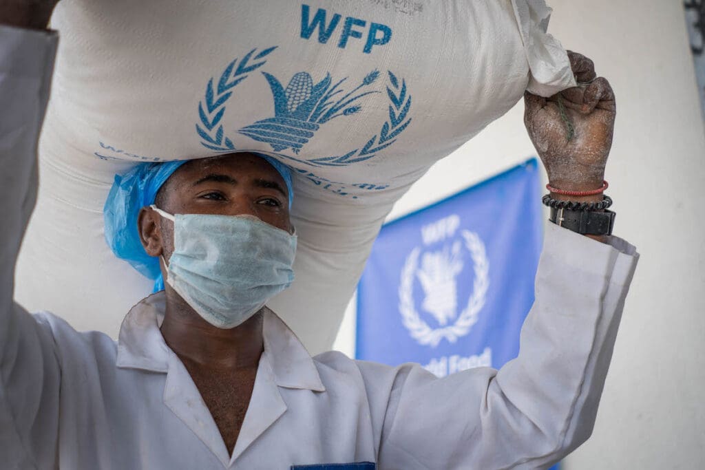 A masked worker carries a bag of food on his head