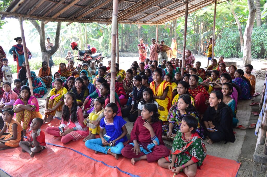 A large group of young girls dressed in colorful clothes sit together on the floor.