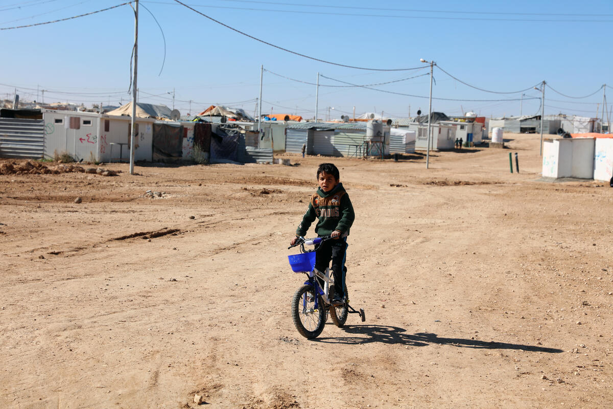 boy riding bicycle on dusty road in refugee camp