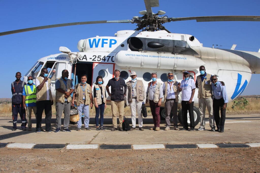 A group of WFP workers stand in a line in front of a transport helicopter.