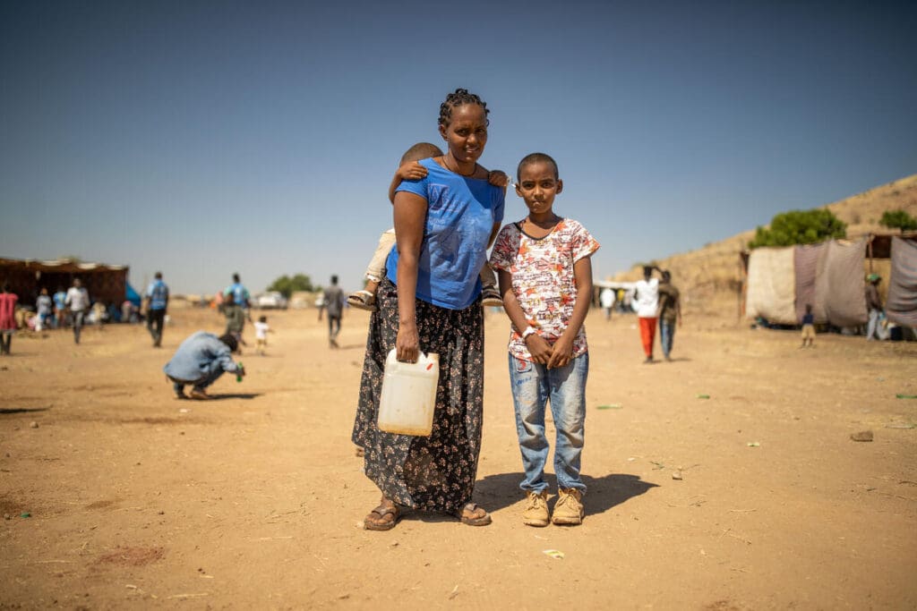 A mother stands outside with her baby and son.