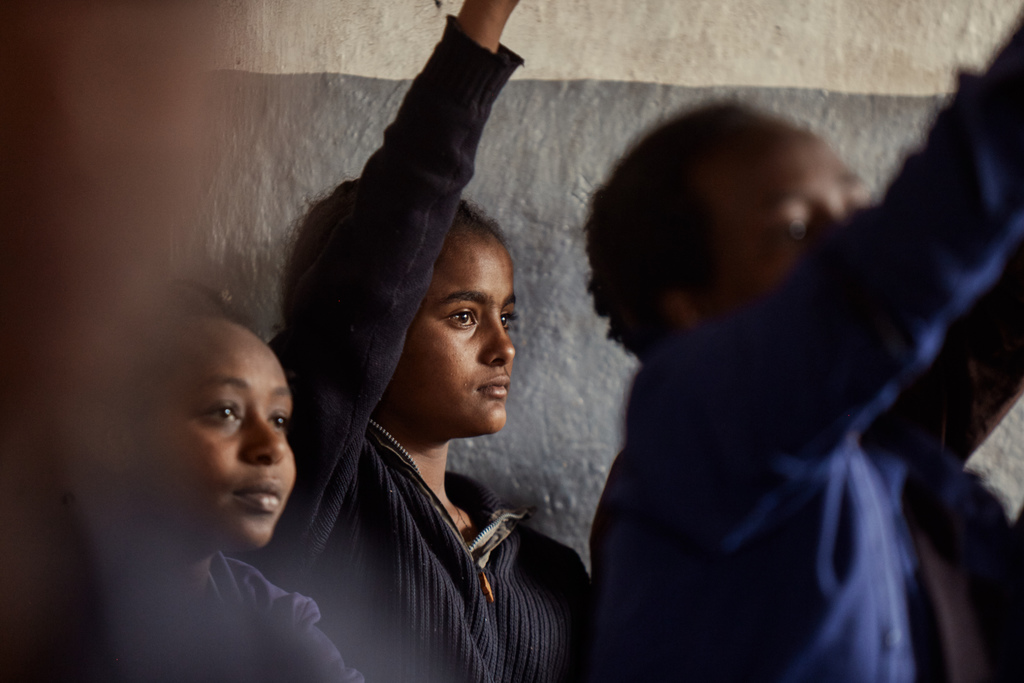 Schoolgirls in uniform raise their hands in class