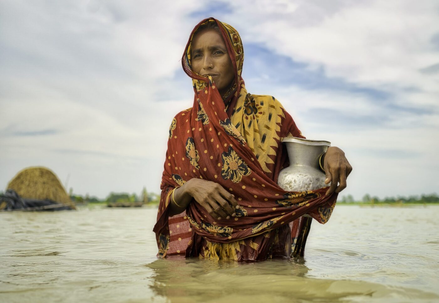 a woman carries a jug of water through flooded waters