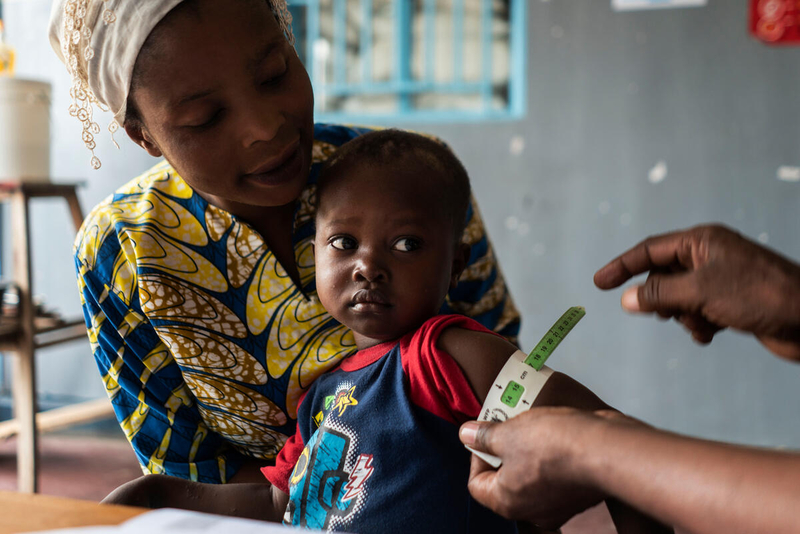 a little boy sits on his mother's lap while his arm is measured