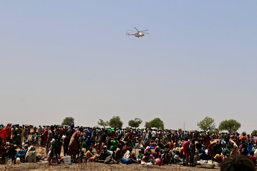 A WFP helicopter flies over a crowd of people.