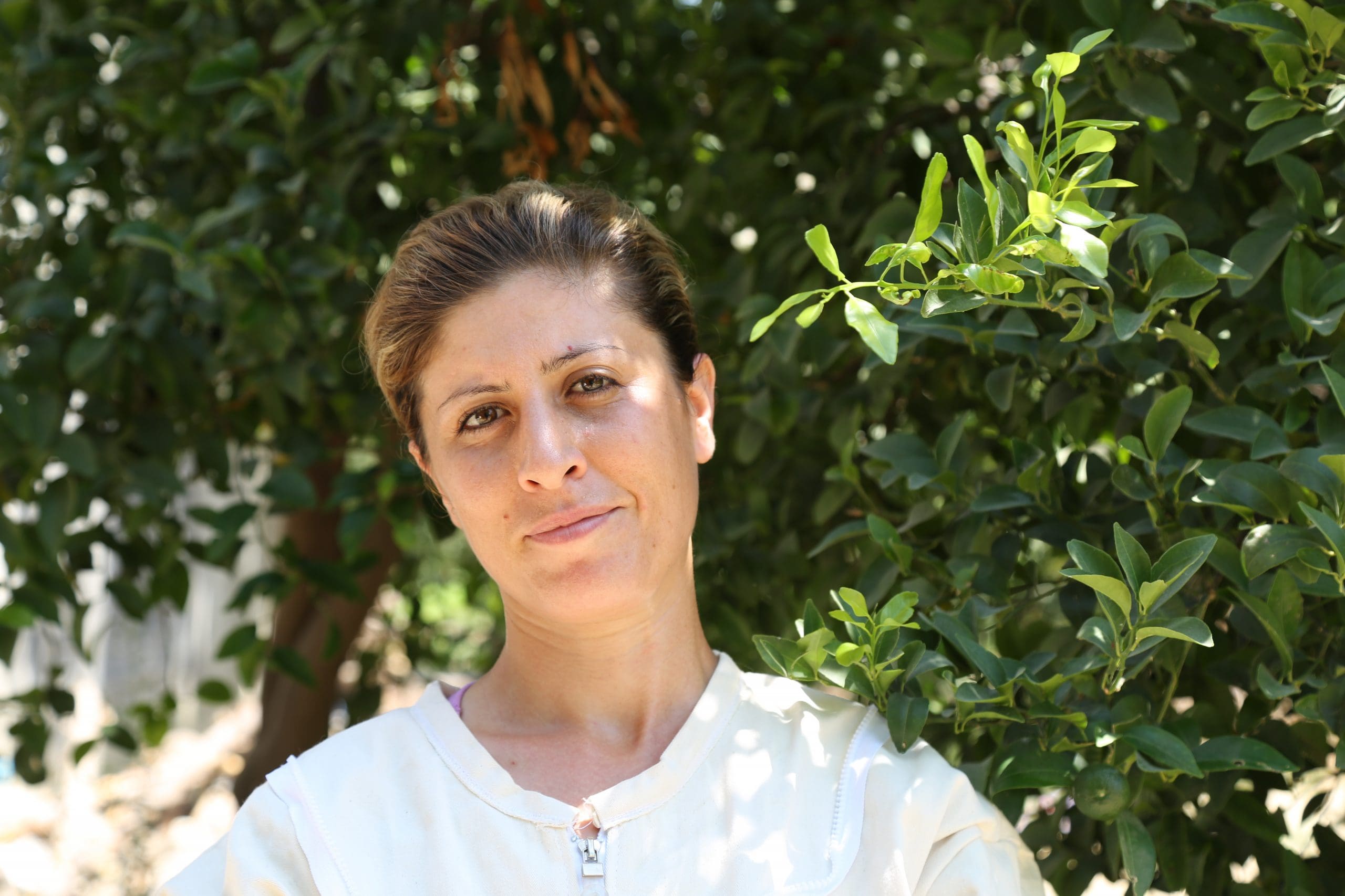 a woman in white shirt stands in front of trees