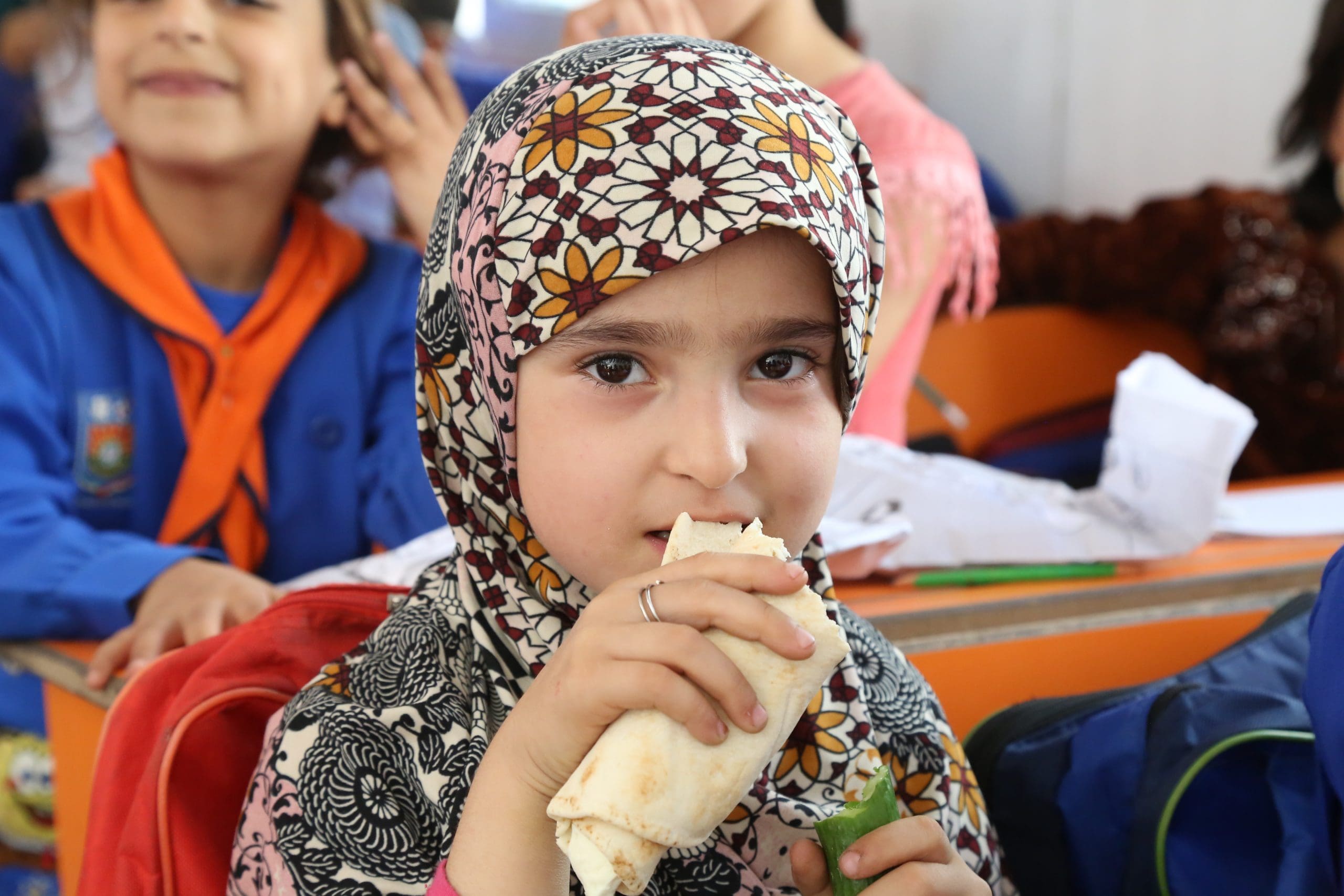 a young girl in colorful headscarf bites sandwich