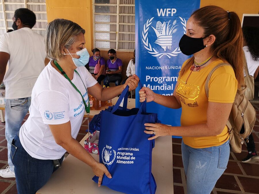 woman in white shirt handing over bag of food to woman in orange shirt