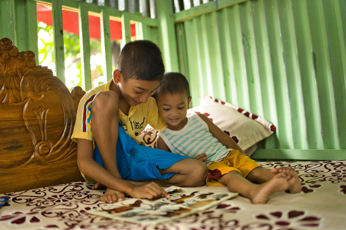 two boys smiling and reading on a bed