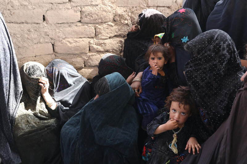 women and children huddled against brick wall