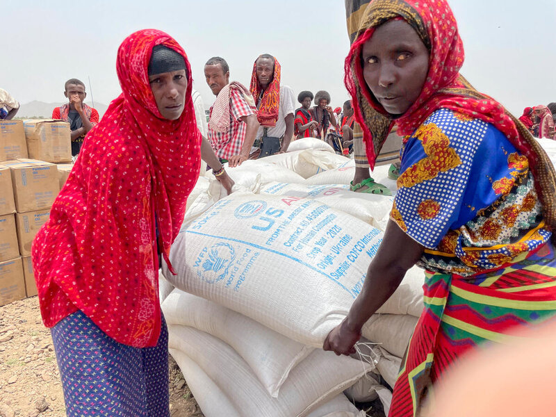 two women in colorful clothes and headscarves carrying bag of food