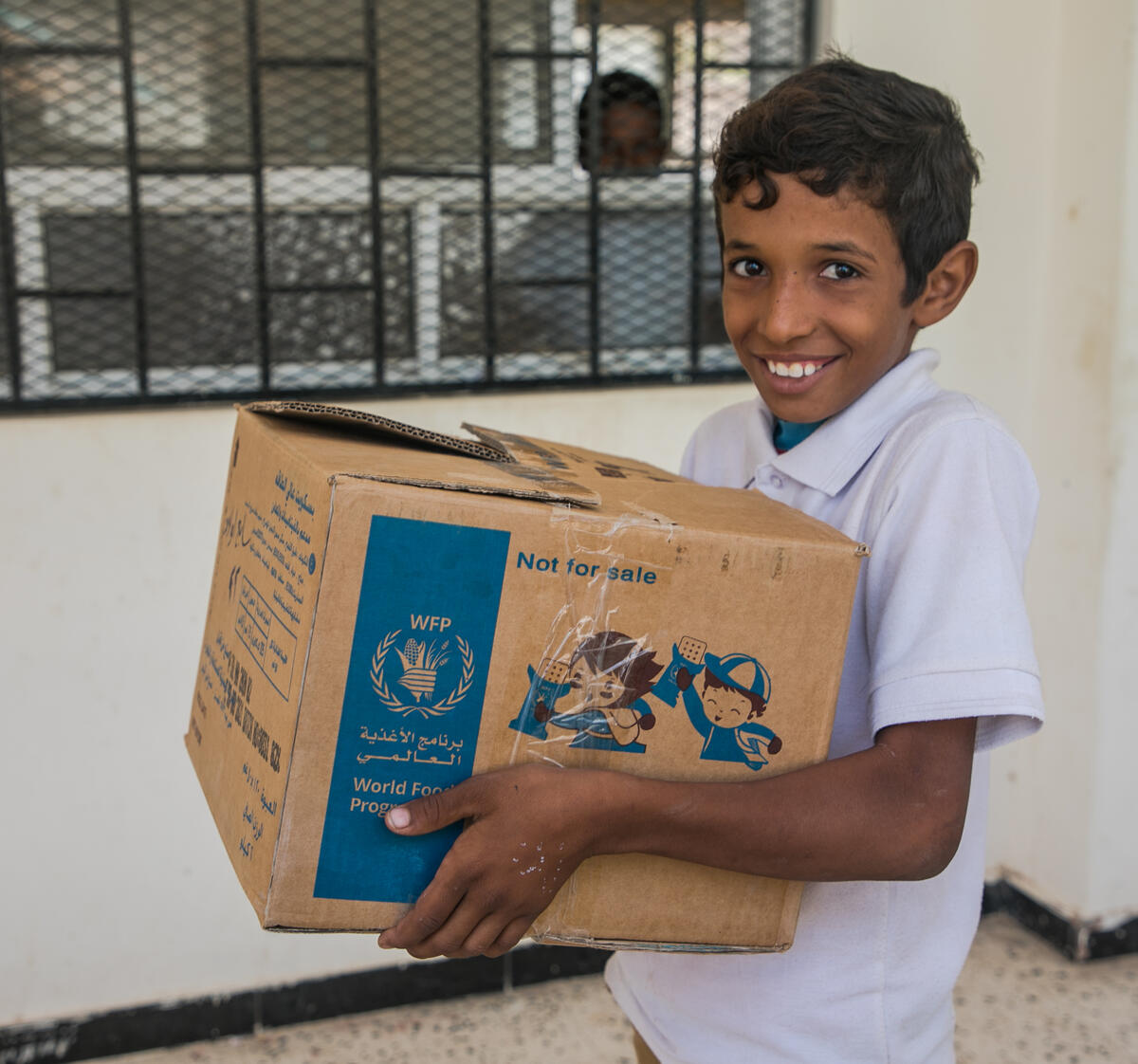 boy smiling and carrying WFP box of food