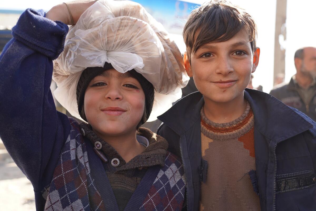 two boys smiling, one holding bread on his head