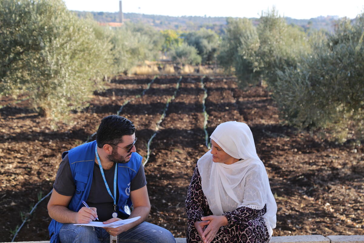 man in WFP vest speaks to woman in white headscarf in garden