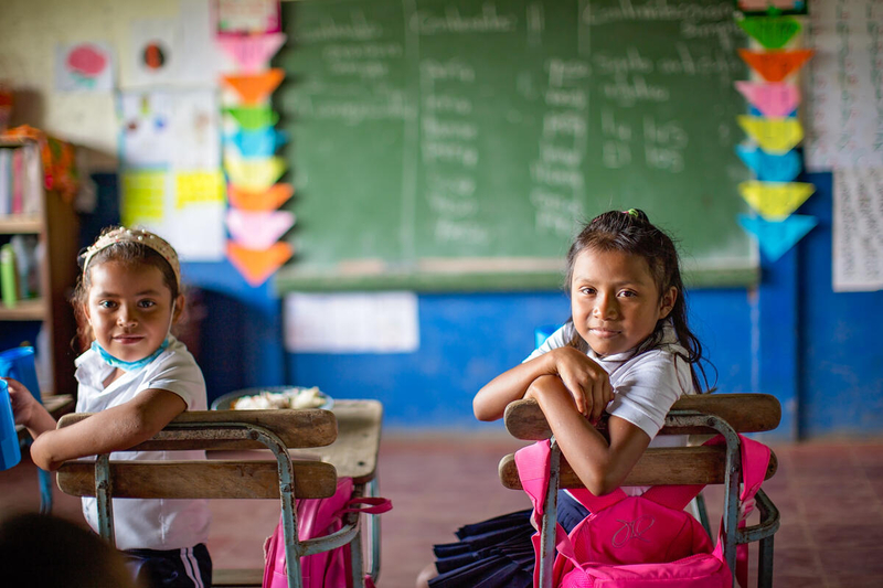 two schoolgirls sitting at desks in classroom