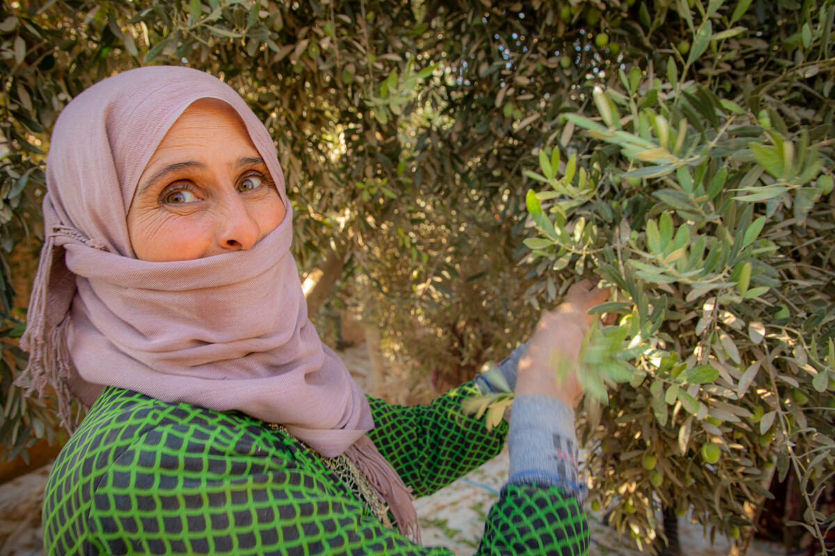 woman in purple headscarf and green shirt by tree