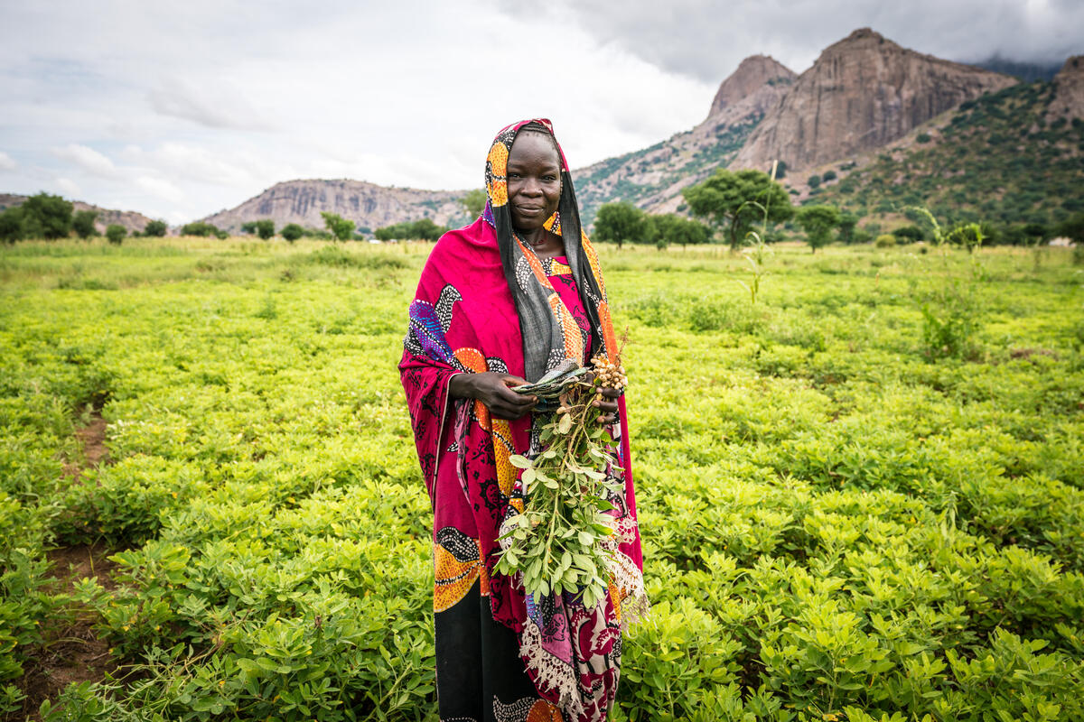 woman in pink headscarf holding vegetables in lush, green field