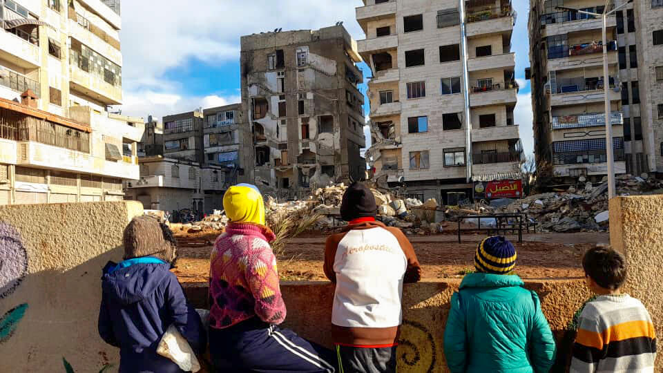 residents walk along damaged buildings following the earthquake in Hama