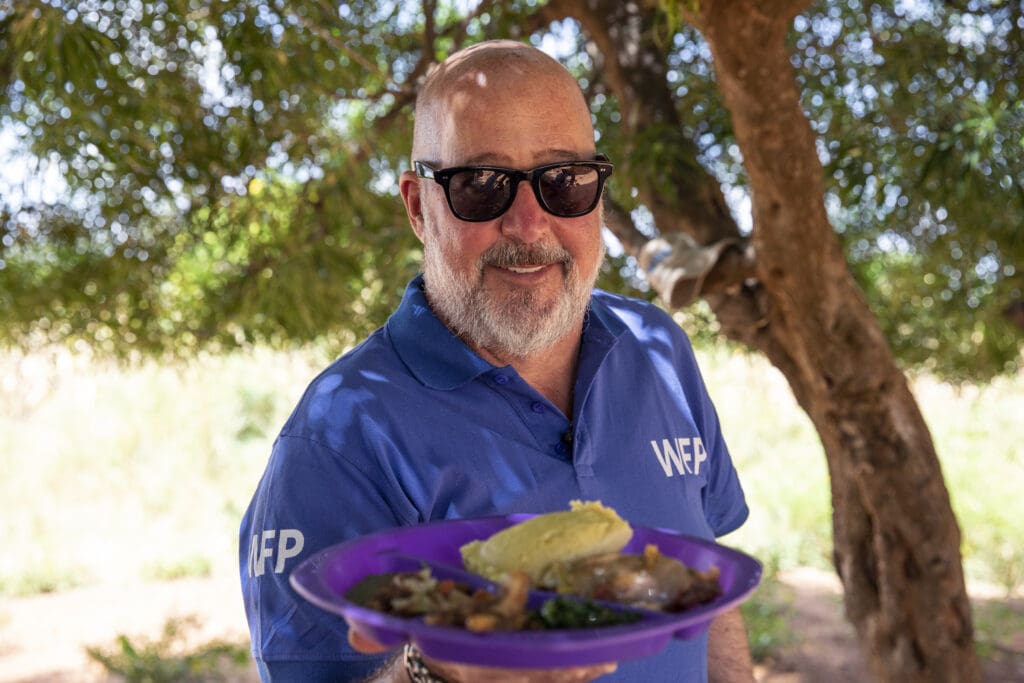 Andrew Zimmern holds plate of food in Zambia