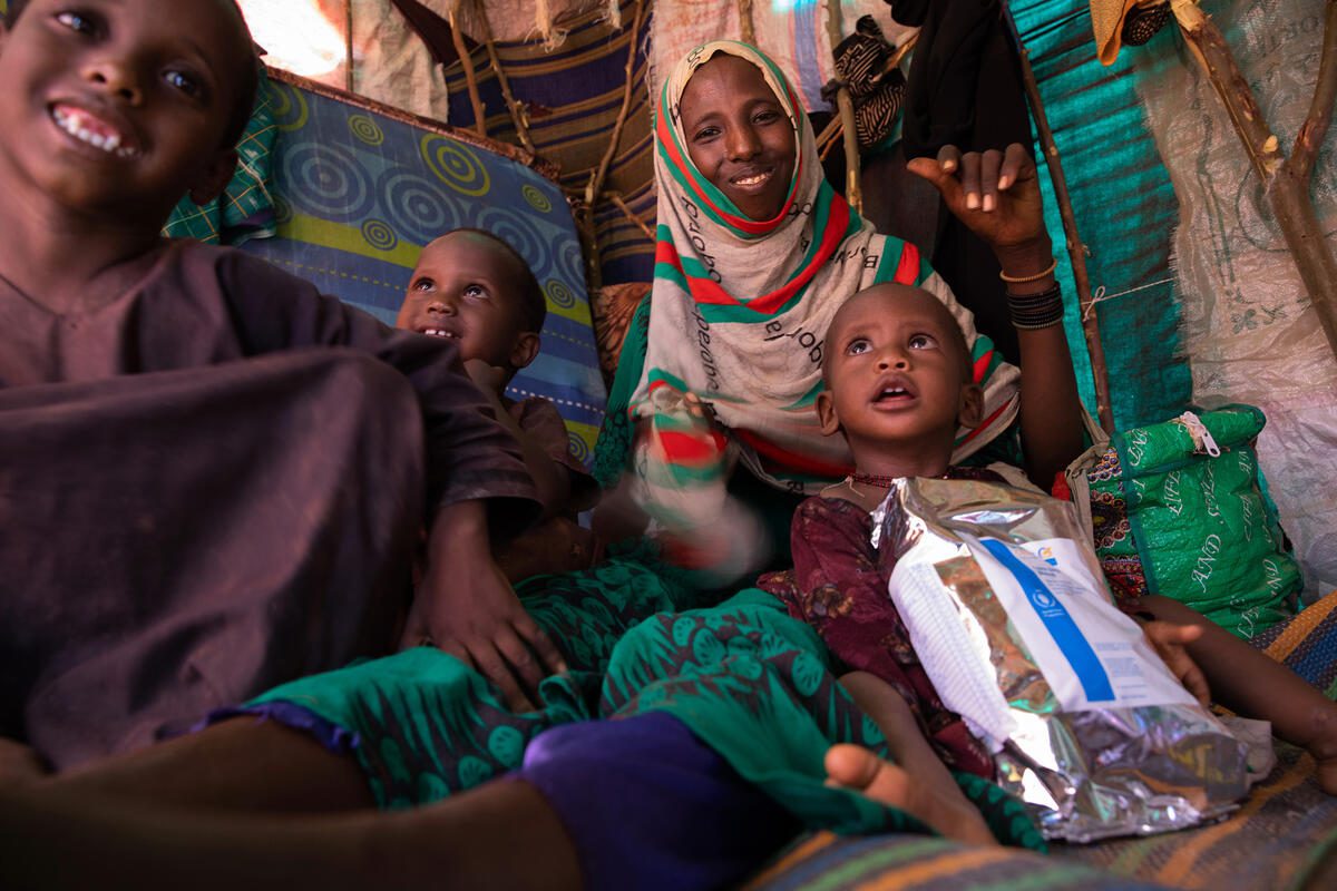 In this photo Mido poses with three of her children (From left to right - Mariam, aged 7, Shamsa, aged 4, and 12 month old Fatun) inside the small shelter they now call home in an IDP camp in Kabasa, Dolow. Also pictured is a bag of super cereal which is part of the nutritional supplementation the receive from WFP.
After a forth consecutive year of drought and increasing security concerns the family left the settlement where they lived and made their way to Dolow. It was a brutal month-long journey - barefoot and only with the clothing they wore. Along the way Mido lost one of her five children to hunger and he was buried enroute. 
Mido said, “We left our home because we had nothing left – we just had drought and hunger.” 
The family now live in a small dome-shaped shelter made from a patchwork of fabrics and plastics in the Kabasa IDP camp. Mido shares cooking utensils with her mother and siblings who have a larger shelter next door to theirs. 
The shelter is in a new extension to the camp, that has developed with the influx of new arrivals fleeing the drought.
Mido’s youngest daughter Fatun suffers from moderate acute malnutrition and they have been referred to the health clinic to receive WFP funded nutrition supplements (plumpy’sup and super cereal) to keep malnutrition at bay