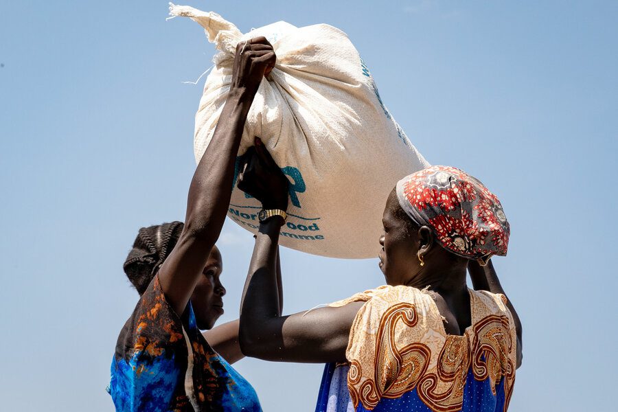 Two woman lift a WFP bag of food